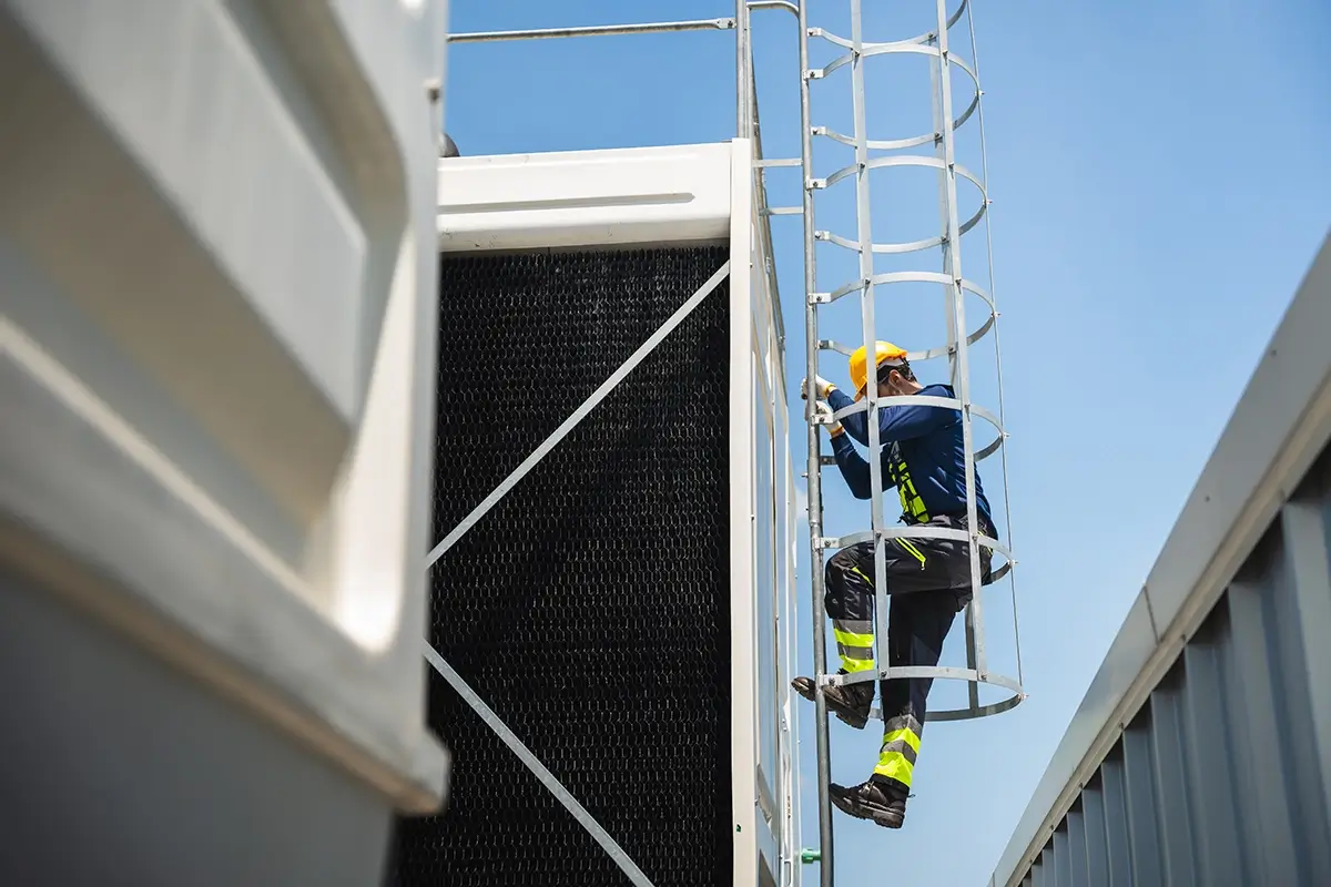 Technicien équipé d'un casque et d'un harnais gravissant l'échelle d'accès à une installation industrielle