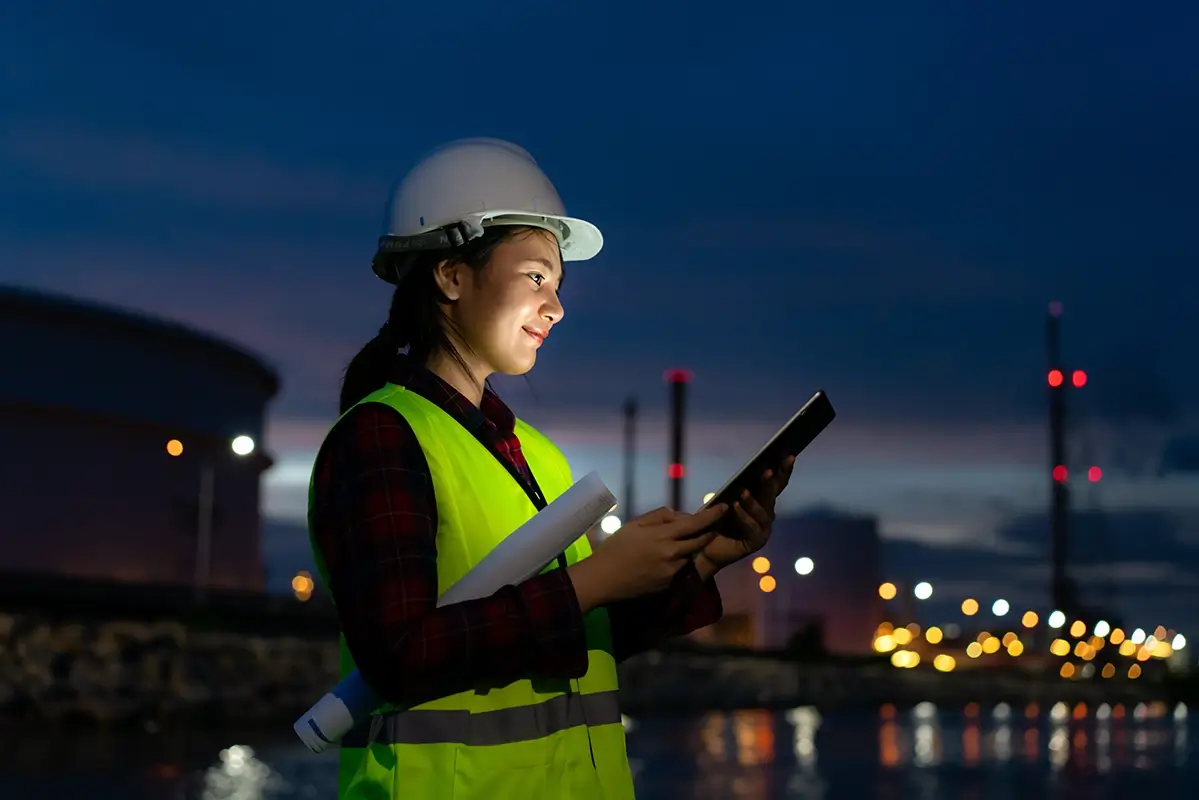 Technicienne consultant un rapport de contrôle sur tablette devant un site industriel