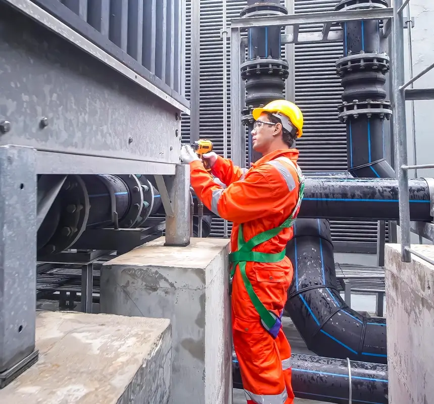 Technicien en combinaison orange intervenant sur un réseau de tuyauteries industrielles