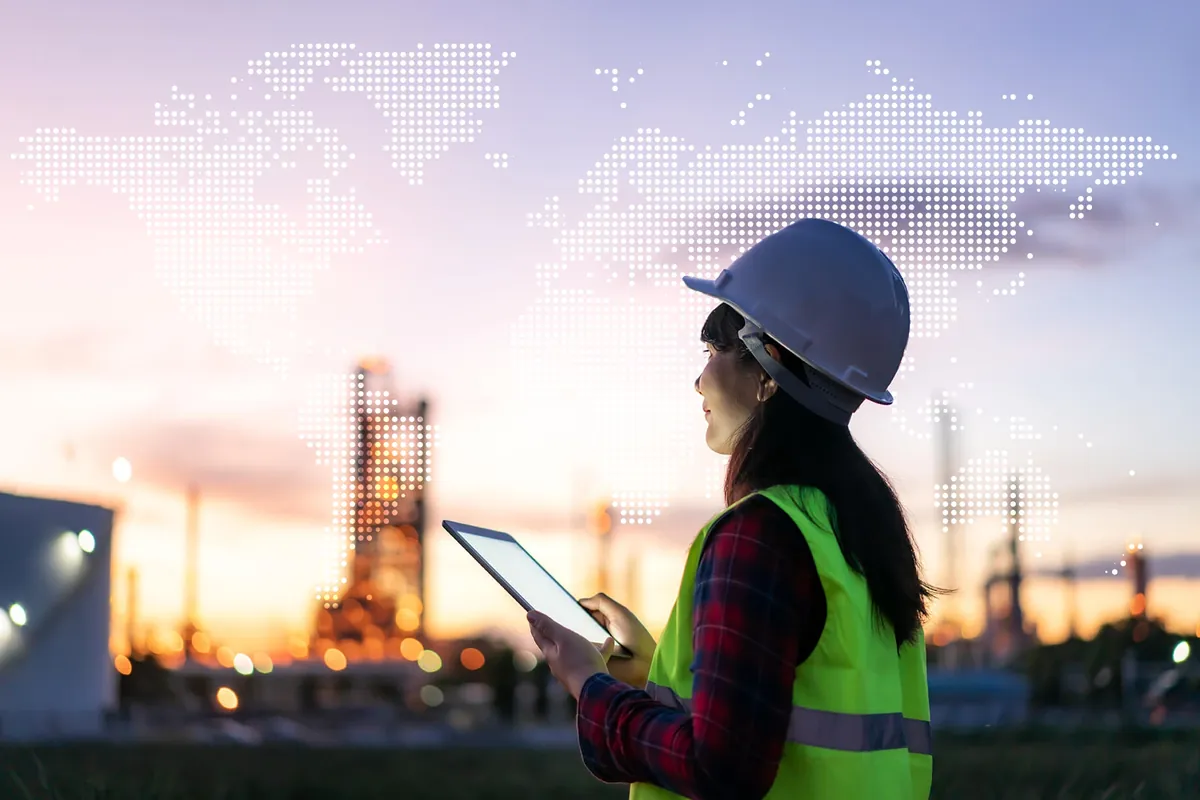 Responsable conformité consultant une tablette devant un site industriel, sur fond de planisphère