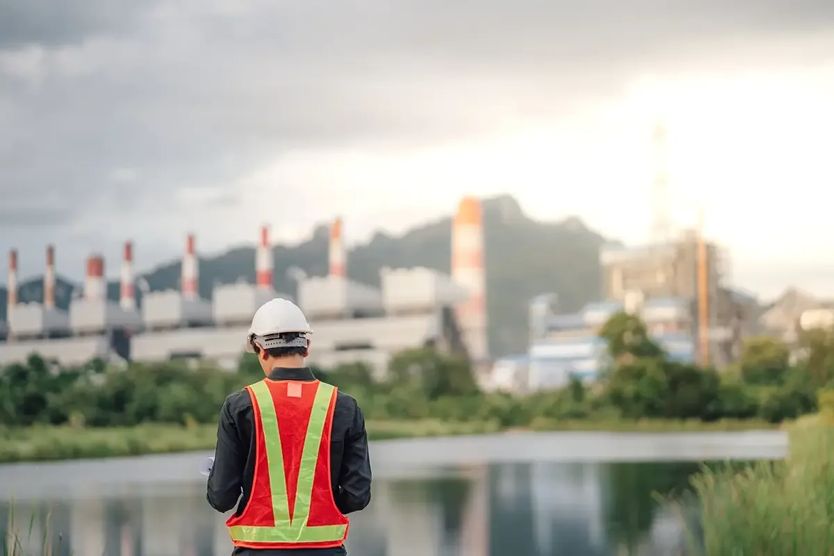 Technicien en gilet haute visibilité face à un site industriel bordé d'un plan d'eau
